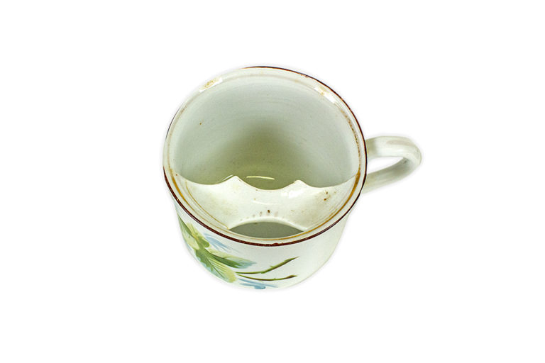 Tea cup with a red rim and floral design. Inside the cup, near the rim, sits a strip of porcelain to protect the moustache from getting wet while drinking