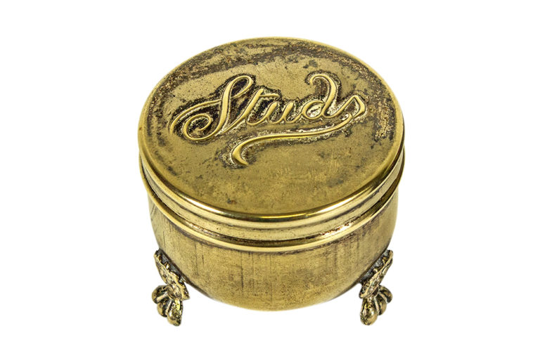 A metal contain with several small feet elevating it off the surface with the word 'Studs' written in cursive on the metal lid