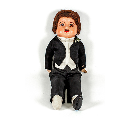 Doll with short brown hair and moustache wearing black suit with fake flower in buttonhole