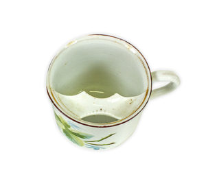 Tea cup with a red rim and floral design. Inside the cup, near the rim, sits a strip of porcelain to protect the moustache from getting wet while drinking