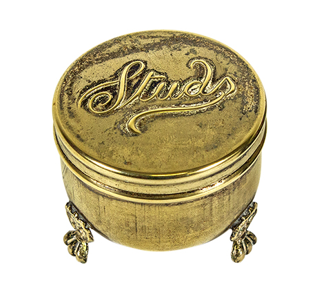 A metal contain with several small feet elevating it off the surface with the word 'Studs' written in cursive on the metal lid